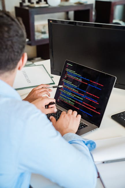 A close-up of a computer screen displaying lines of colorful programming code, predominantly featuring syntax highlighting in bright green, red, blue, yellow, and white against a dark background. The 